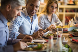 African American entrepreneur talking to his colleagues during lunch break in restaurant.